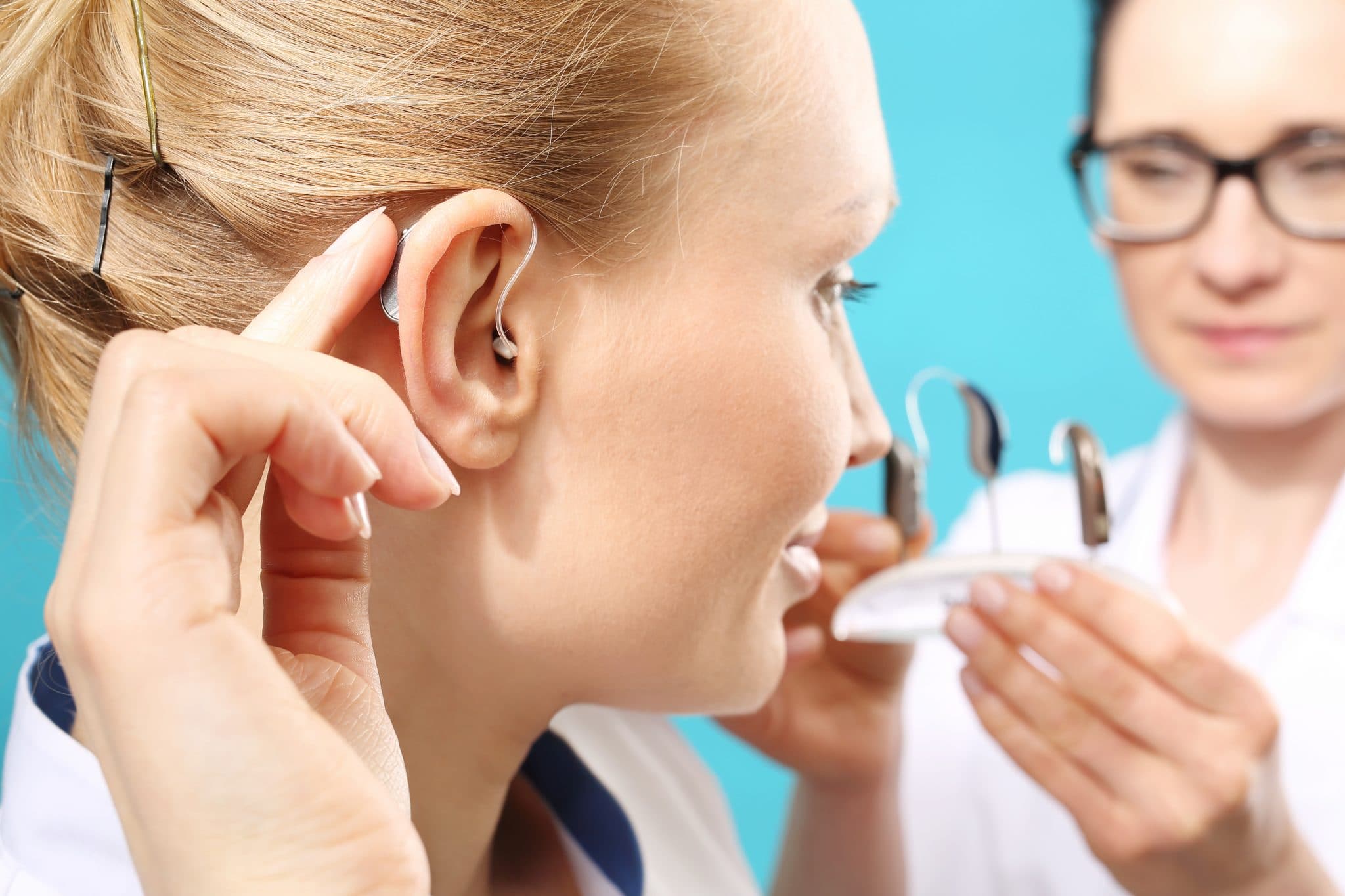 Femme ayant des problèmes d'audition insérant un appareil auditif avec l'aide d'un professionnel de la santé.