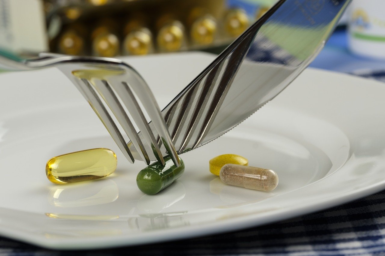 Une fourchette en position au-dessus d'une assiette contenant une sélection de complément alimentaire, privilégiant les capsules de Vitamine D.