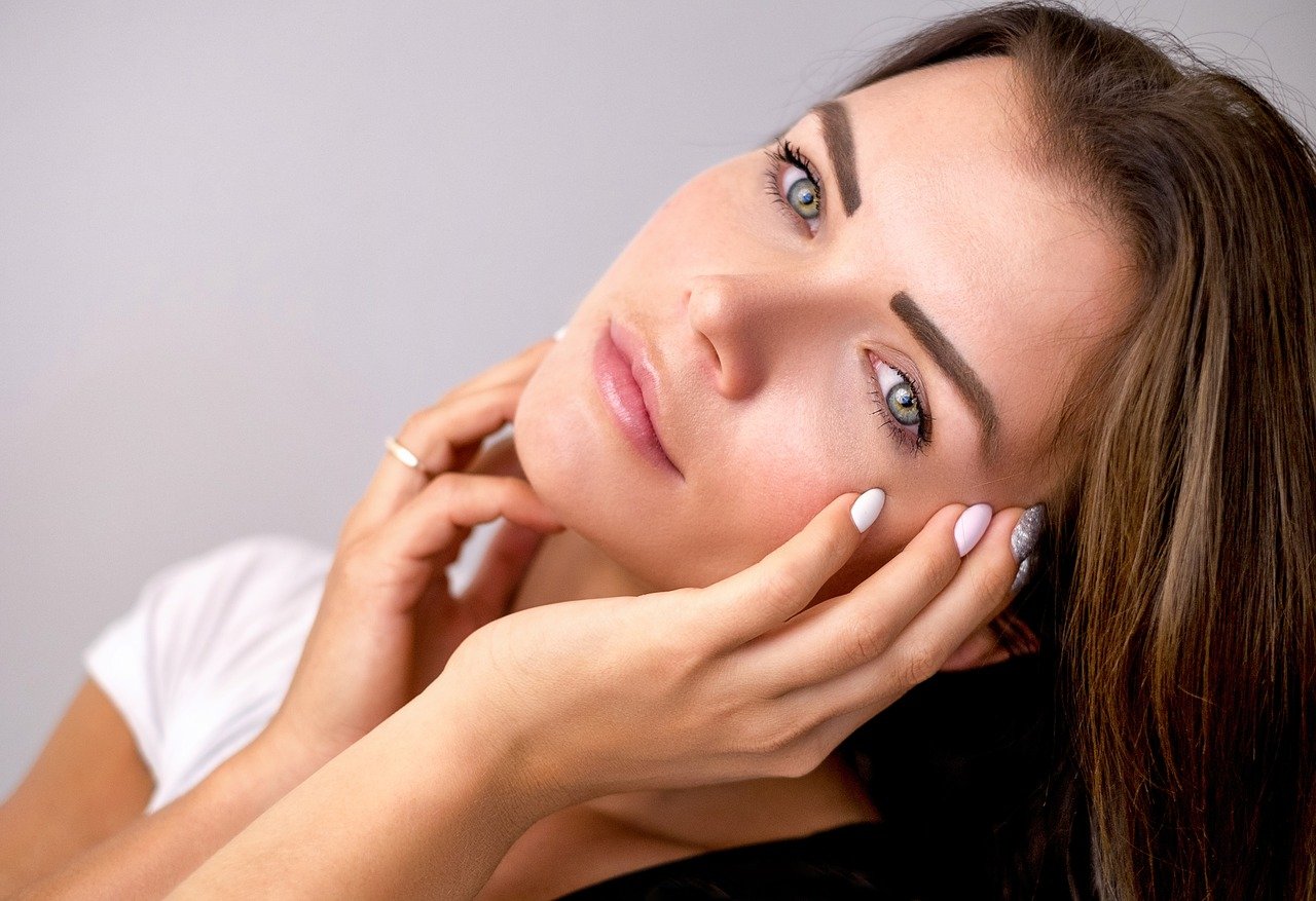 Femme aux yeux bleus posant les mains sur le visage, illustrant les meilleures préventions contre les maladies de la peau.