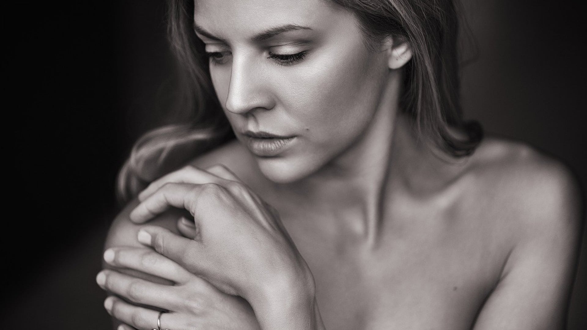 Une femme contemplative, après quarante ans, dans un portrait en noir et blanc, le regard baissé et les mains doucement effleurées.