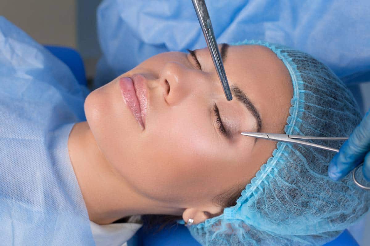 Une patiente subit une intervention esthétique avec un chirurgien utilisant des instruments près de son sourcil.