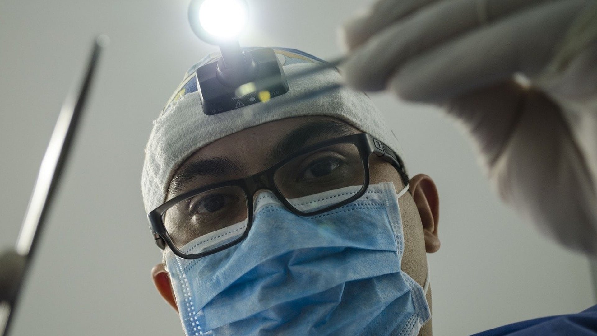 Un médecin de garde, portant un masque chirurgical et une lampe frontale, se prépare à une intervention.