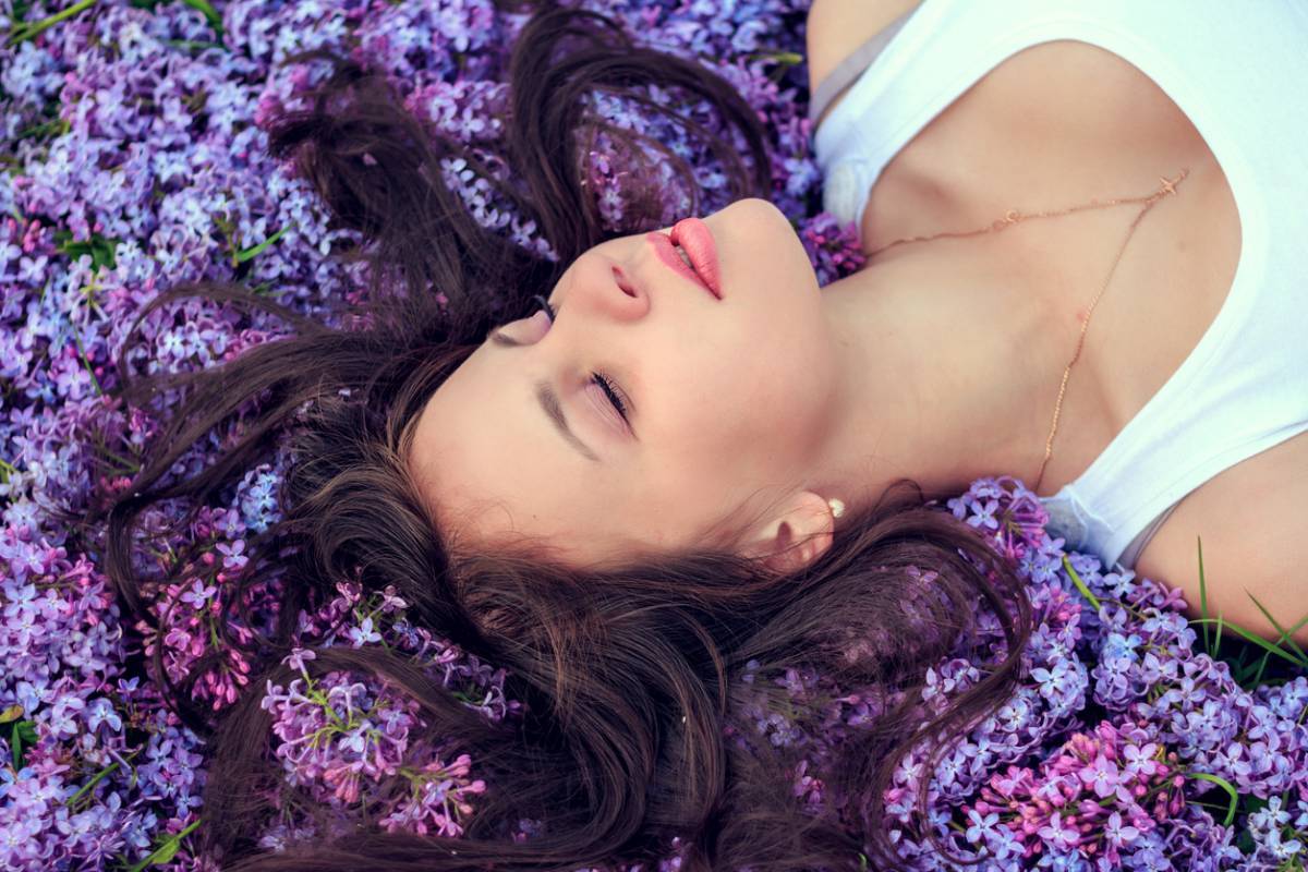 Jeune femme allongée dans un champ de fleurs lilas, incarnant le bon sommeil parmi les plantes.