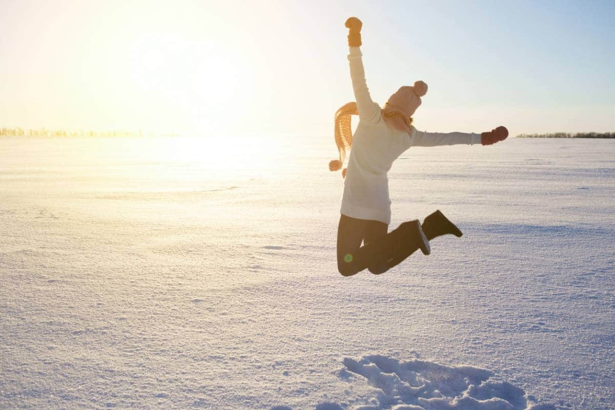 Femme sautant joyeusement dans un paysage enneigé par une journée ensoleillée.