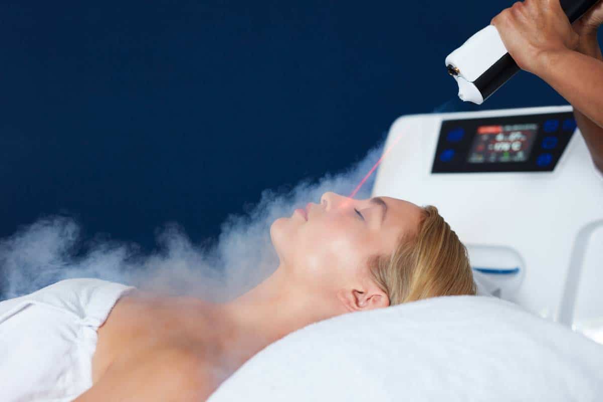 Femme recevant un soin du visage avec un appareil à vapeur dans une clinique de beauté.