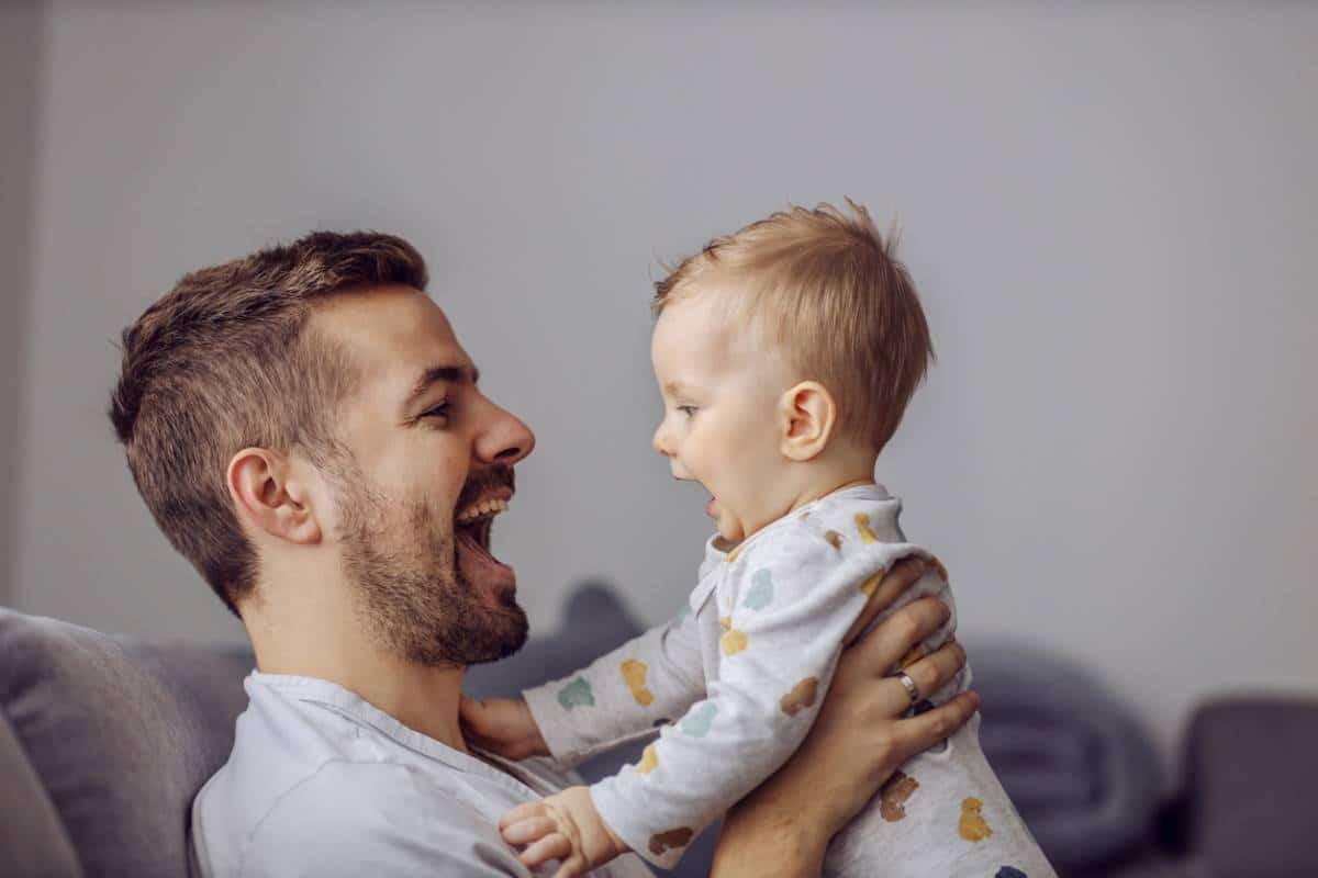 Un homme souriant tenant un bébé qui rit alors qu'il était assis sur un canapé.