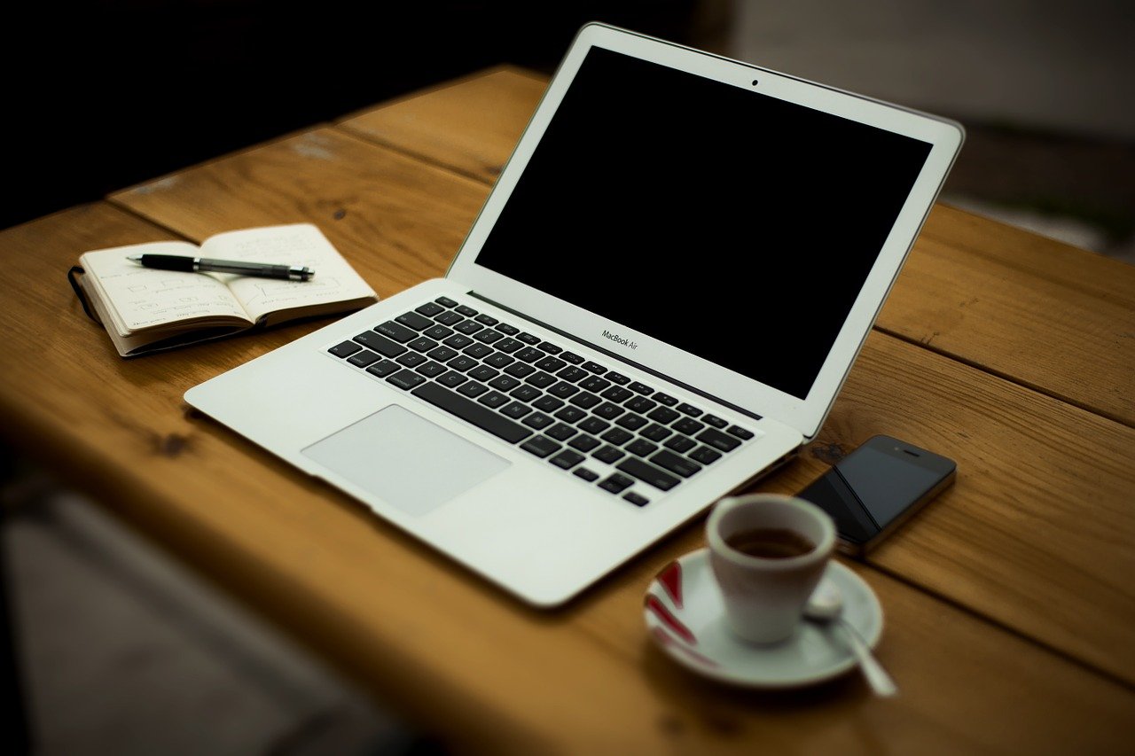 Un ordinateur portable avec un écran vierge, un smartphone, un bloc-notes avec un stylo et une tasse de café sur une table en bois.