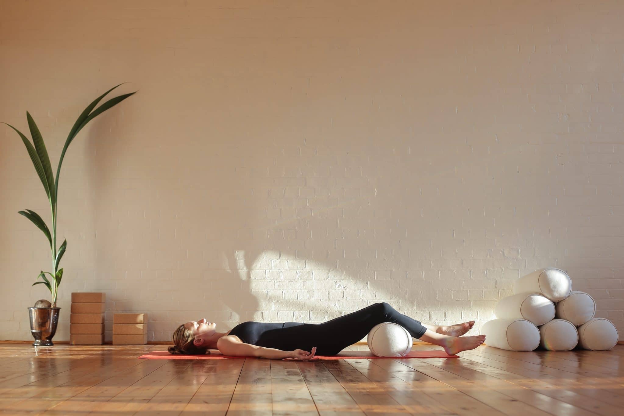 Une personne est allongée sur un tapis de yoga dans une pièce ensoleillée, avec des accessoires de yoga à proximité pour des postures visant à soulager
