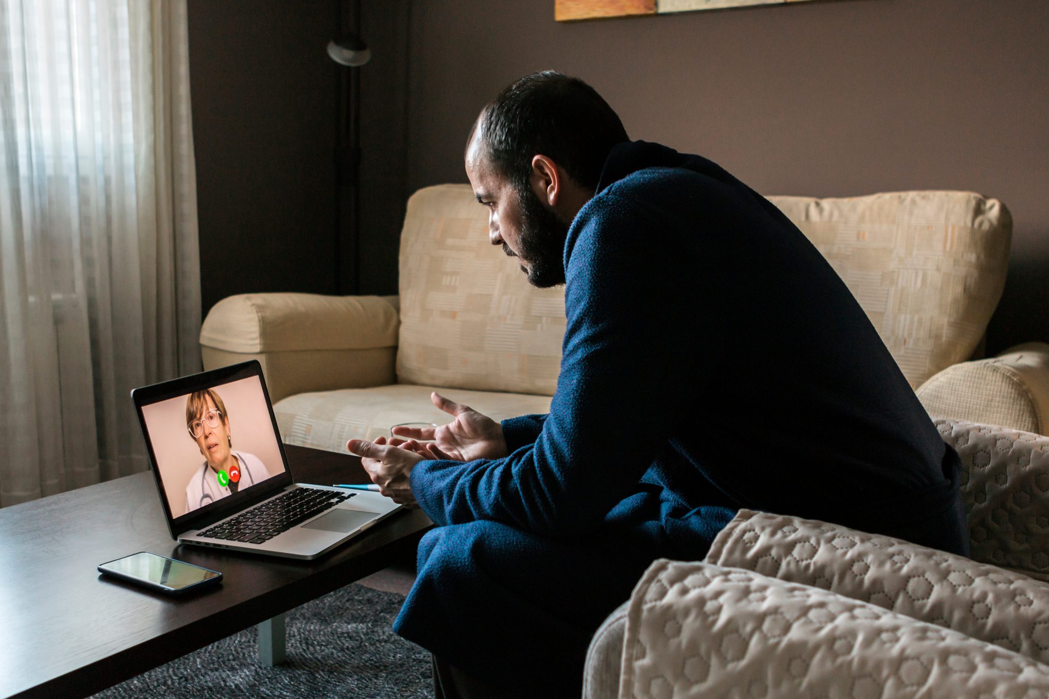 Homme en peignoir passant un appel vidéo sur un ordinateur portable dans une pièce faiblement éclairée.