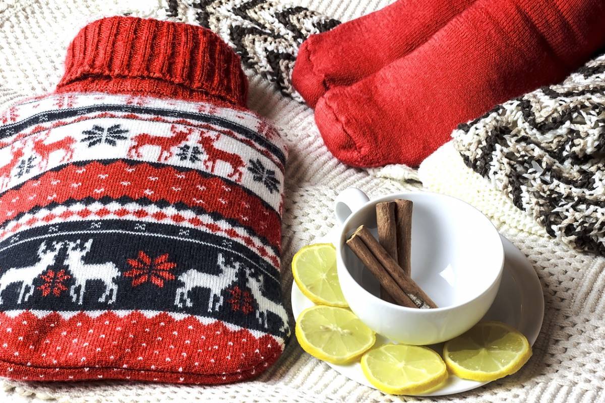 Des accessoires d'hiver douillets avec une bouillotte, des chaussettes tricotées, une écharpe, des tranches d'agrumes et des bâtons de cannelle.
