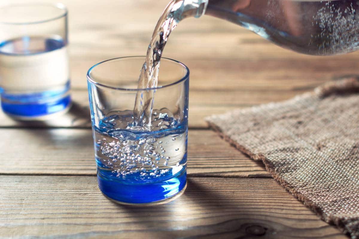 Verser de l'eau dans un verre transparent sur une table en bois.