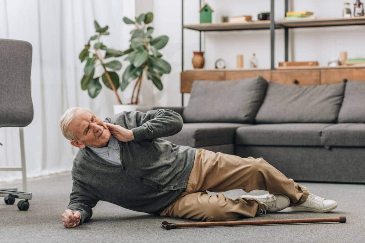 Homme âgé allongé sur le sol et se tenant le cou, semblant ressentir un inconfort ou une douleur.