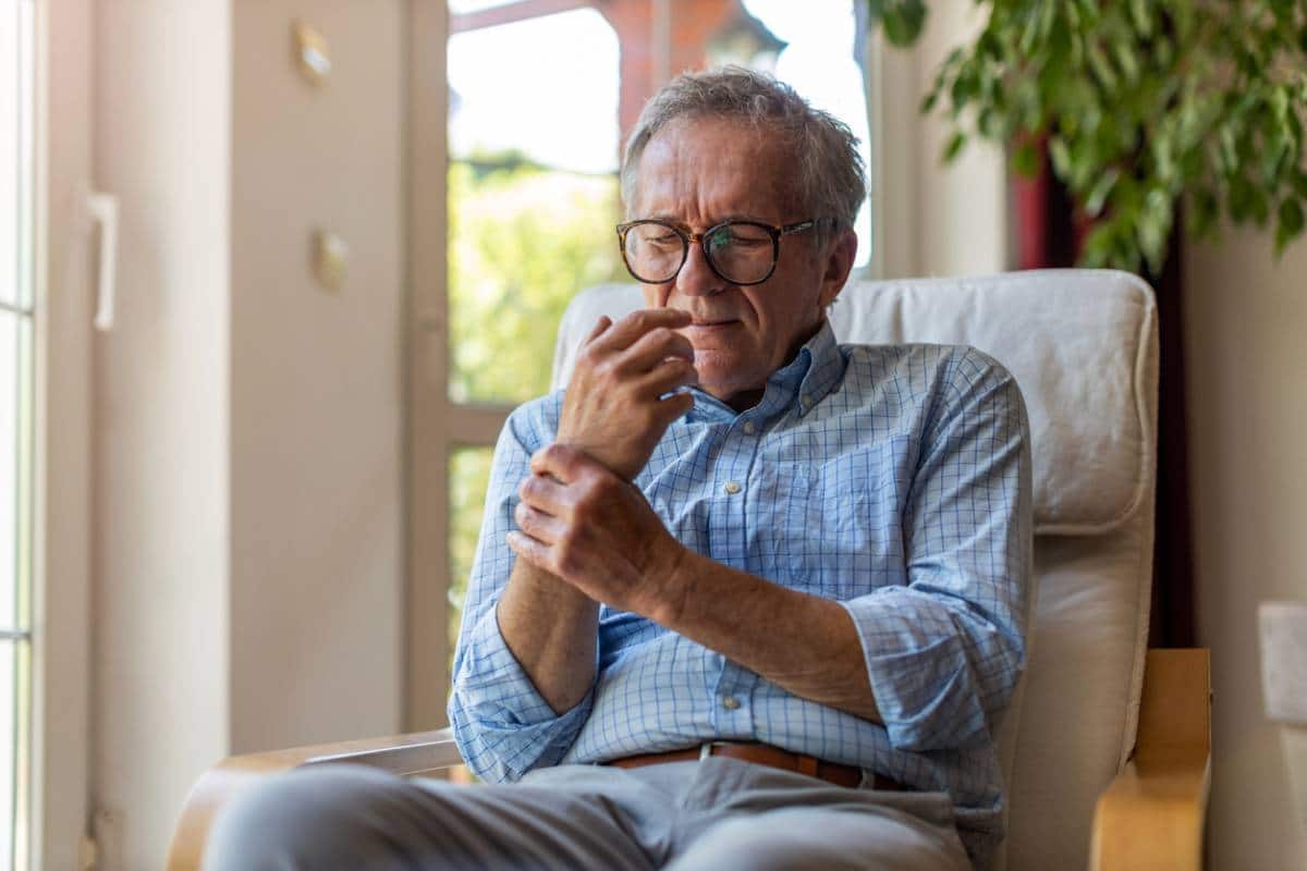 Un homme âgé assis à l'intérieur regardant pensivement une tasse de café, un appareil de téléassistance à sa portée pour plus de sécurité.