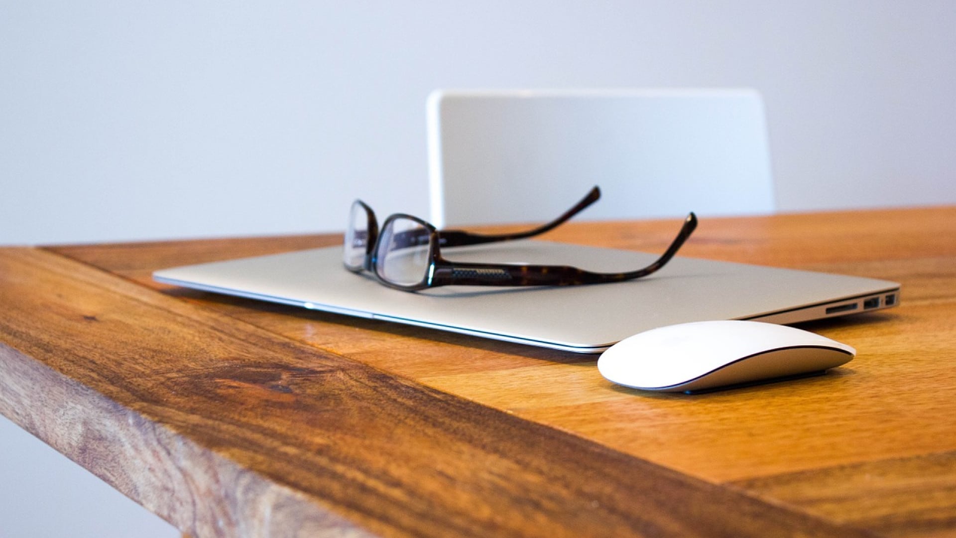 Une paire de lunettes posée sur un ordinateur portable fermé à côté d'une souris sans fil sur une table en bois.