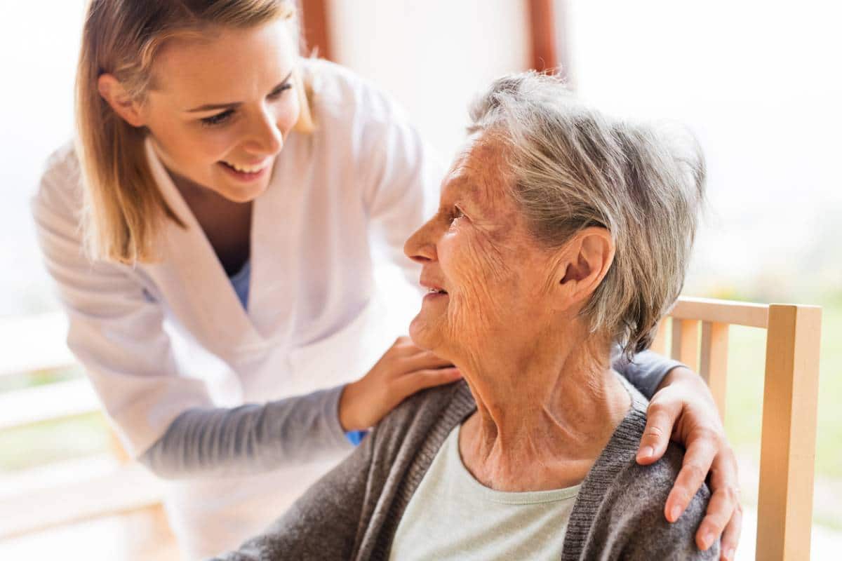 Un professionnel de la santé sourit à une femme âgée tout en posant une main sur son épaule dans un geste réconfortant.