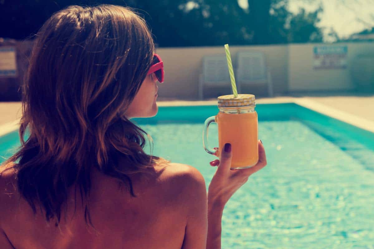 Femme tenant un pot Mason avec une boisson détox d'été au bord de la piscine.