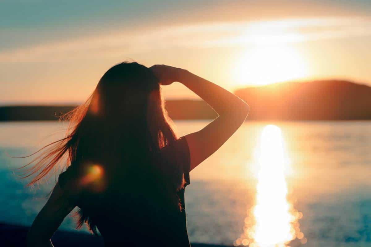 Femme regardant le coucher de soleil sur l'eau, contemplant sa personnalité.