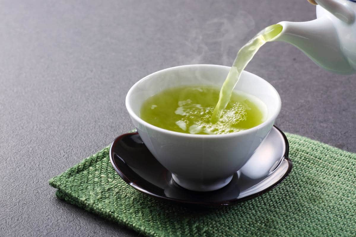 Verser du thé vert dans une tasse sur un tapis vert.