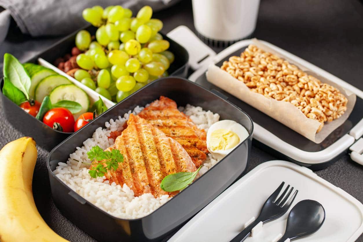Un repas équilibré avec du saumon grillé, du riz, des légumes, des noix, des fruits et un œuf à la coque servi dans un plateau compartimenté.