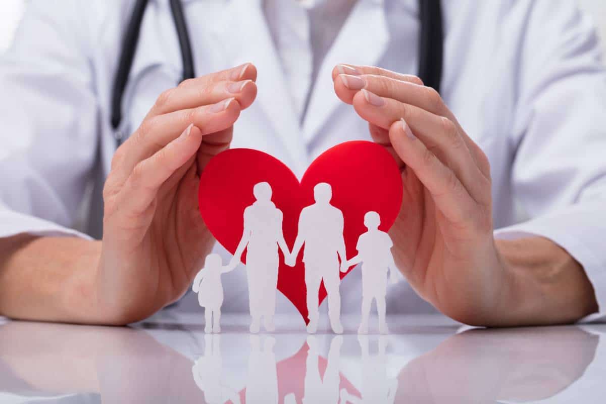 Un professionnel de la santé tient une famille découpée en papier dans un cœur rouge, symbolisant les soins médicaux et la protection des familles.