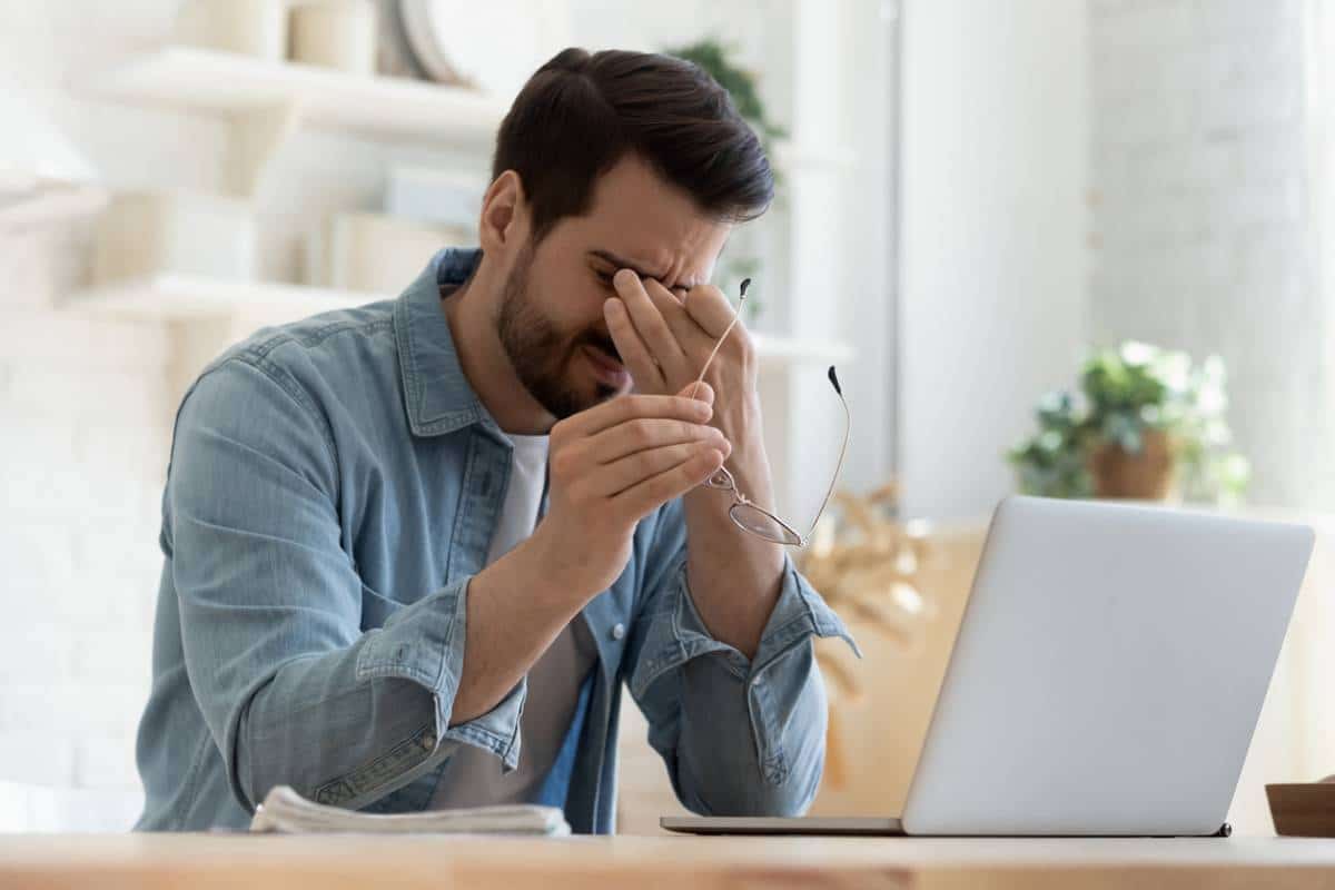 Homme se sentant stressé ou souffrant de maux de tête lorsqu'il travaille sur un ordinateur portable.