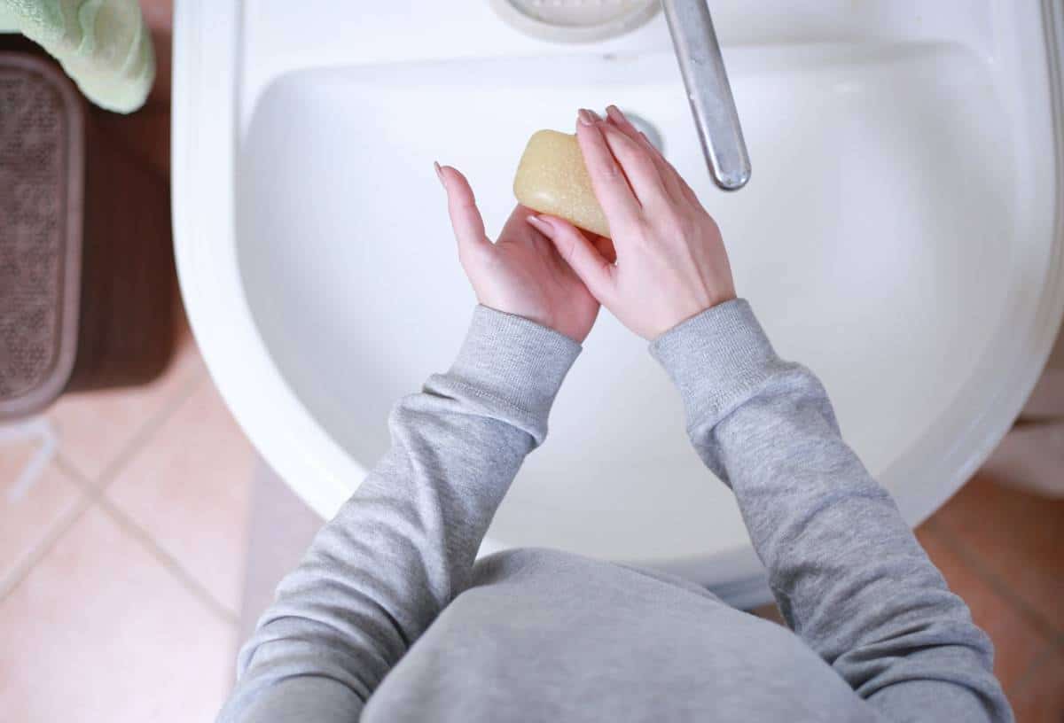 Personne tenant un pain de savon au-dessus d’un lavabo de salle de bain.