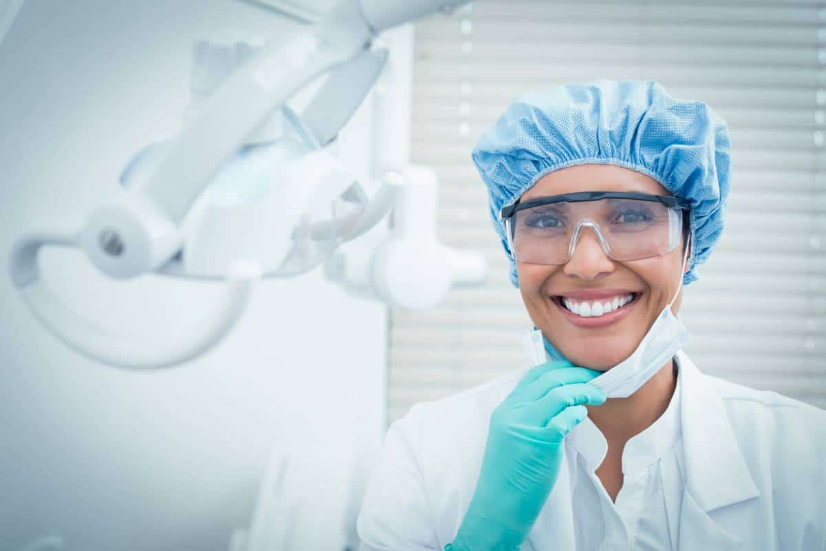 Dentiste en tenue de protection souriant dans une clinique dentaire, services expliqués.