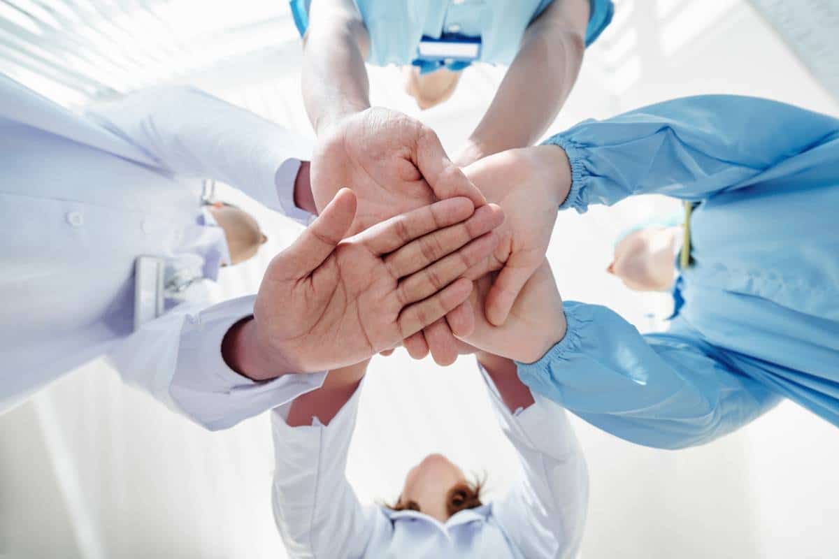 Une équipe de professionnels de la santé empilant les mains pour faire preuve d’unité et de travail d’équipe.