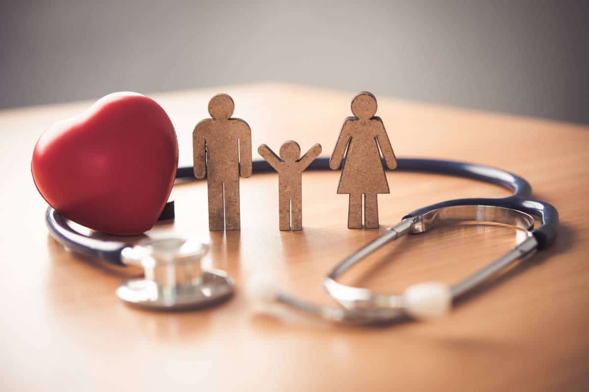 Une figure familiale en bois se tient à côté d’un cœur rouge et d’un stéthoscope, symbolisant les soins de santé et le bien-être familial.