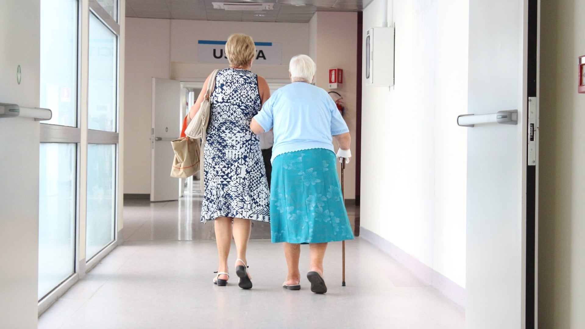Deux femmes marchant dans un couloir d’hôpital, dont l’une utilise une canne.