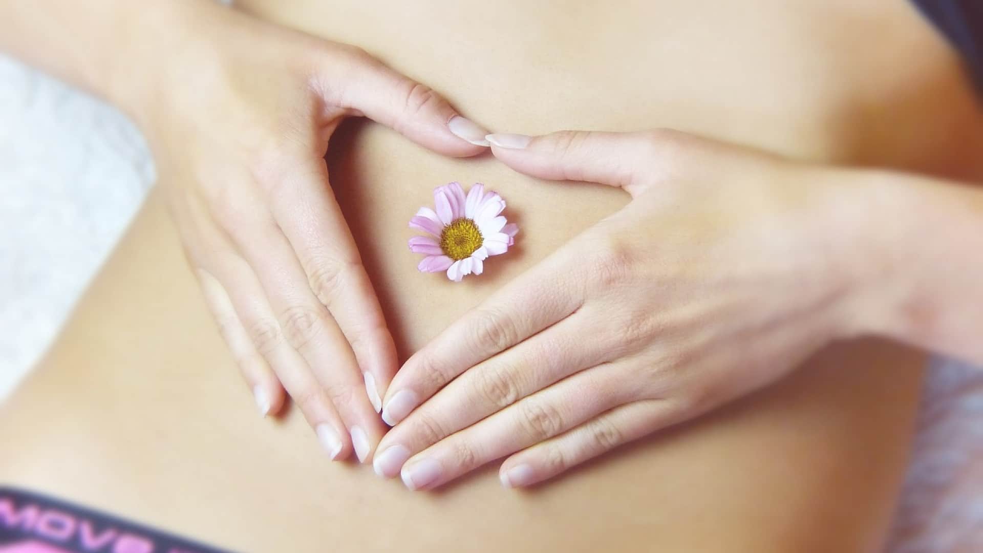Les mains d'une femme formant un coeur sur le ventre avec une fleur au centre.