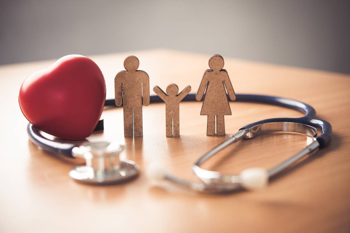Figurines en bois représentant une famille avec un cœur rouge et un stéthoscope sur une table, symbolisant les soins de santé.