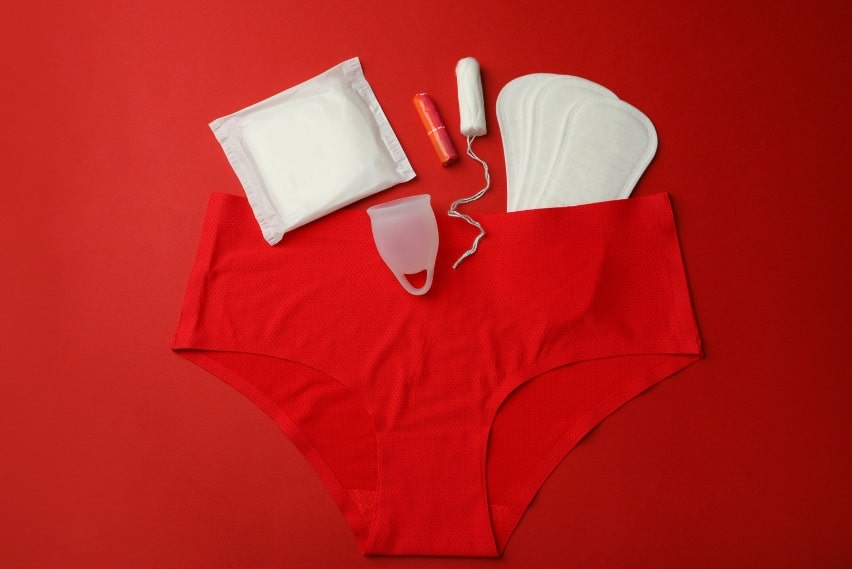 Produits d'hygiène menstruelle disposés sur fond rouge avec une paire de sous-vêtements.