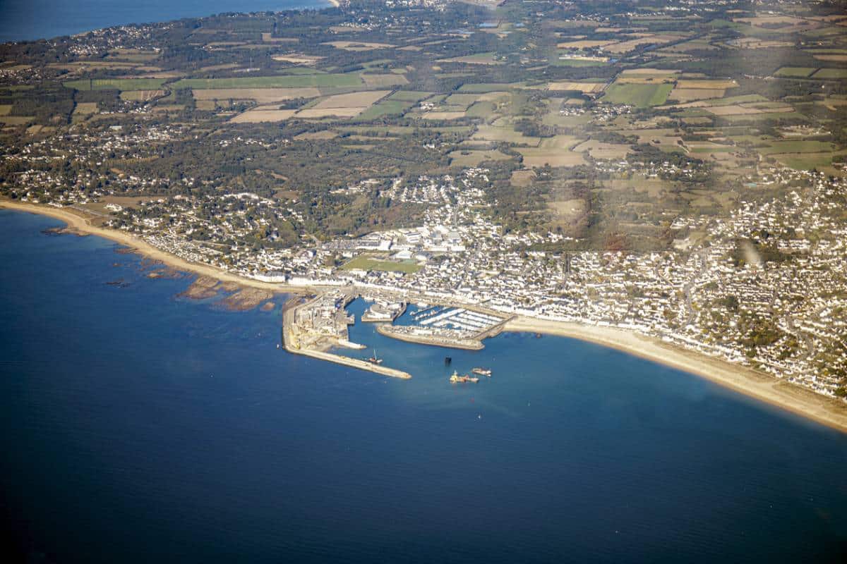 Vue aérienne d'une ville côtière avec un port et des terres agricoles environnantes.