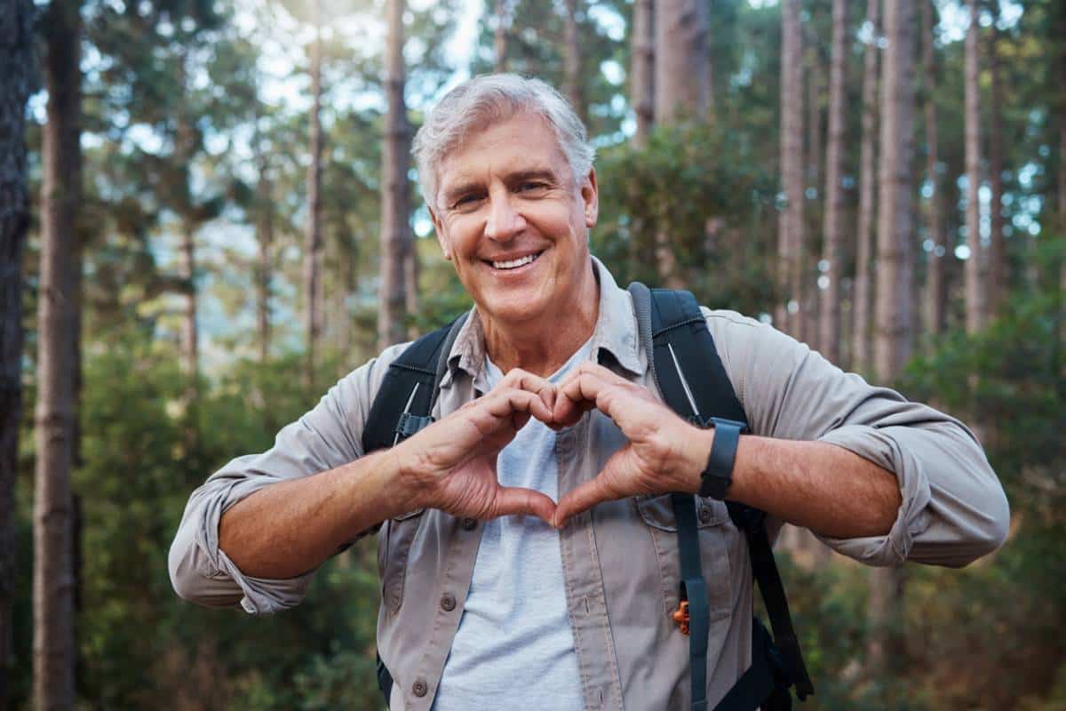 Homme âgé avec sac à dos en forme de coeur avec ses mains dans la forêt.