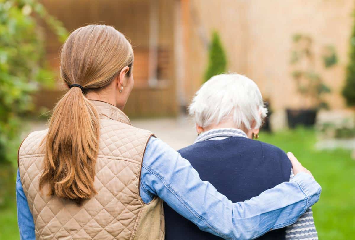 Une femme soutient une personne âgée alors qu’elle marche ensemble à l’extérieur.