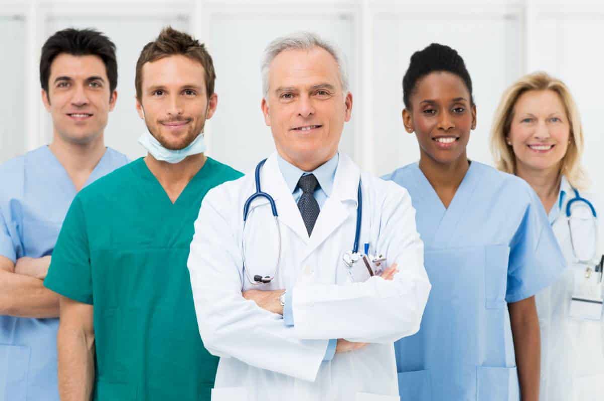 Un groupe diversifié de cinq professionnels de la santé, comprenant des médecins et des infirmières, posant ensemble dans un cadre médical.