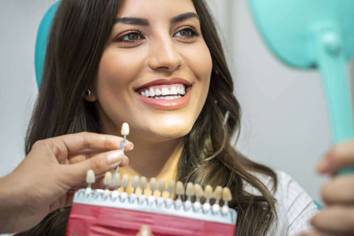Une femme compare la teinte de sa dent avec un nuancier dentaire pour mieux comprendre l'implantologie dentaire.