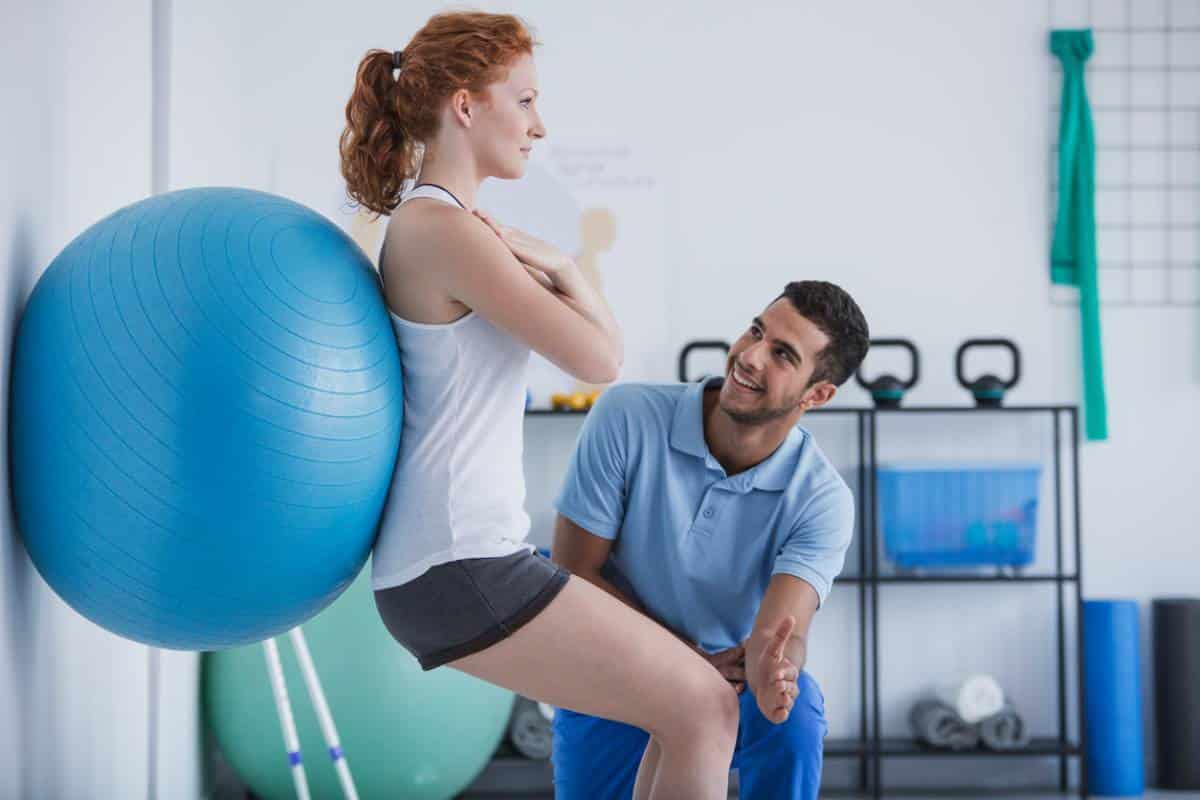Physiothérapeute aidant une femme à faire un exercice à l'aide d'un ballon de stabilité.