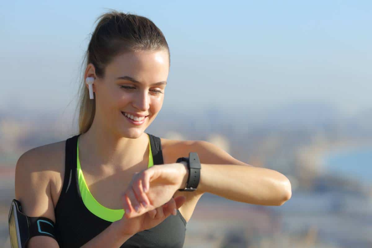 Femme vérifiant sa montre intelligente équipée des dernières fonctionnalités sport 2.0 lors d'une séance d'entraînement en plein air.