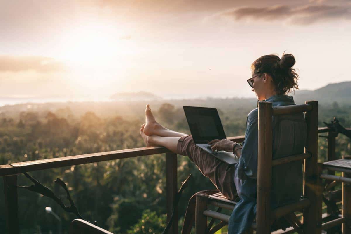 Un employé travaillant sur un ordinateur portable à l'extérieur au coucher du soleil avec une vue panoramique en arrière-plan.