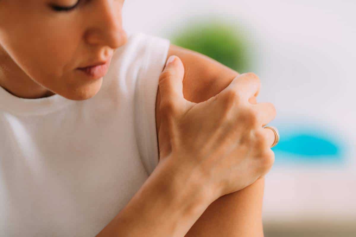 Femme se grattant le bras à cause d'une démangeaison ou d'une irritation, éventuellement liée à un problème d'épaule.
