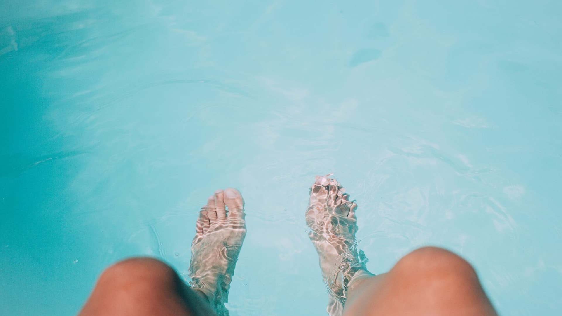 Les pieds hallux valgus de la personne immergés dans l’eau bleue claire de la piscine.