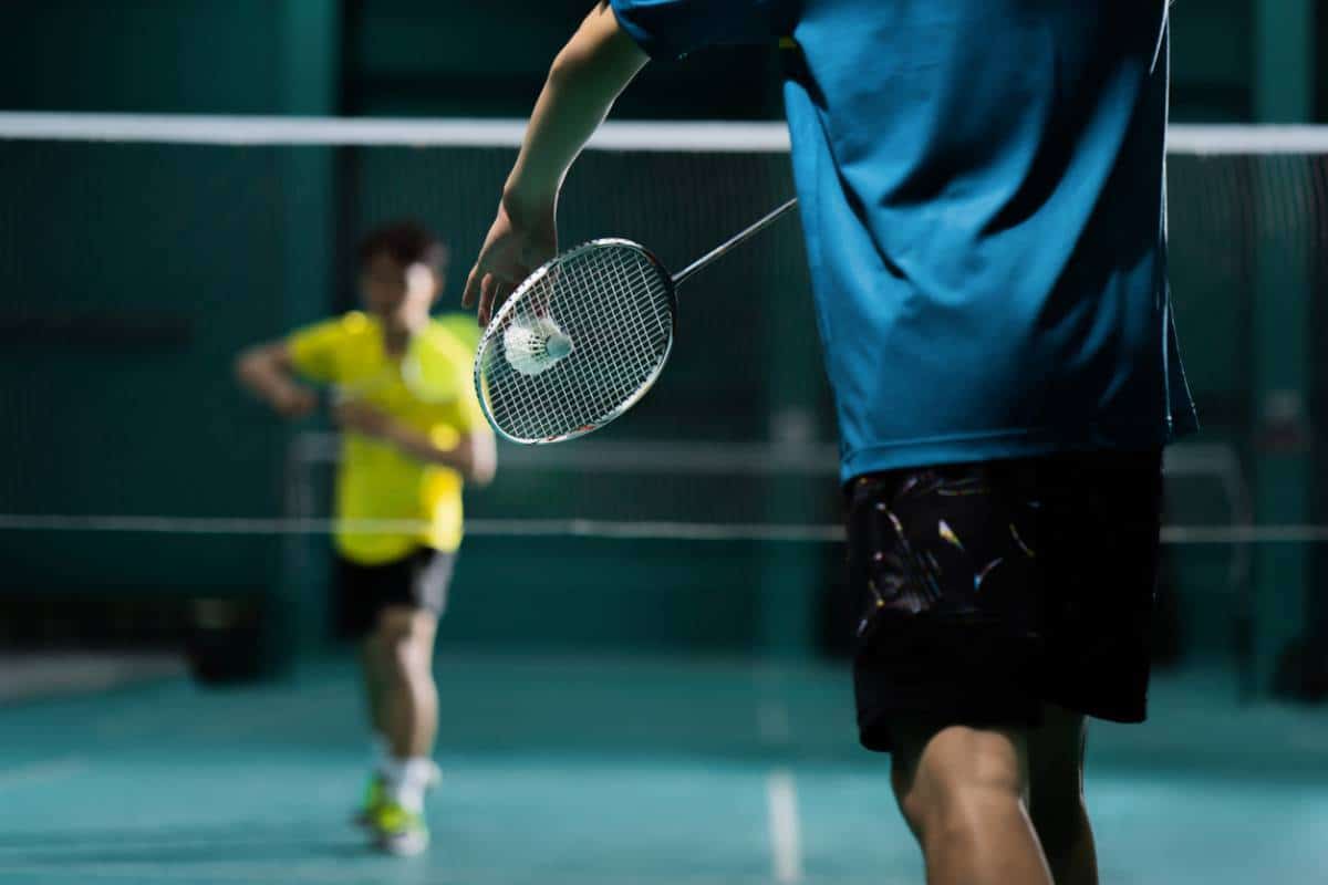 Deux personnes jouant à un match de badminton à l'intérieur, avec un joueur prêt à frapper le volant.