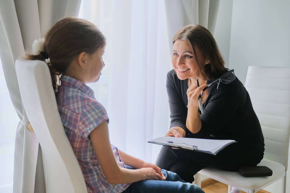 Un thérapeute souriant tenant un presse-papiers écoute attentivement un jeune enfant lors d'une conversation sur les émotions.