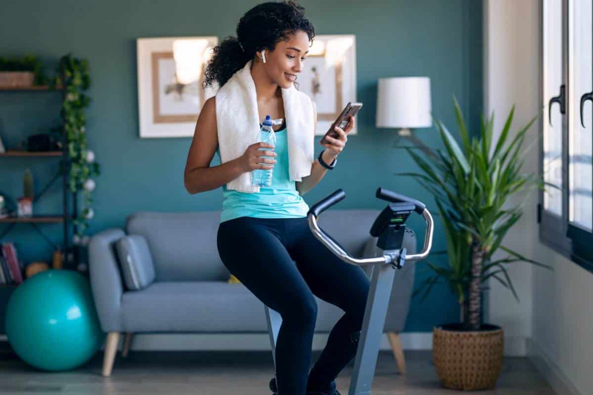 Une femme sur un vélo d'exercice, s'entraînant efficacement tout en utilisant une plateforme en ligne sur son téléphone.