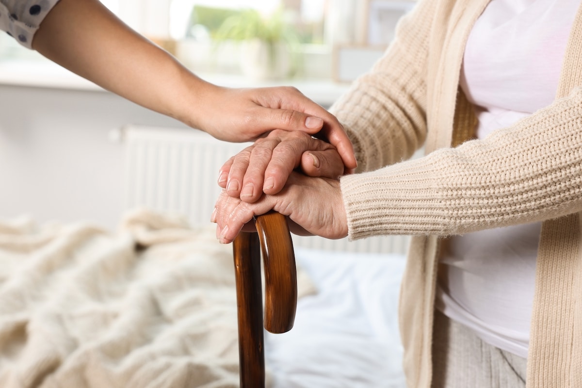 Une femme tient la canne d'une femme âgée sur un lit, favorisant le bien-être des personnes âgées.