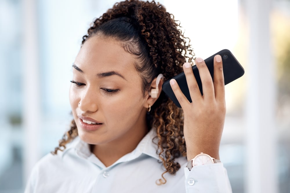 Une femme aux cheveux bouclés utilise une application sur son téléphone portable pour améliorer sa qualité de vie quotidienne et ajuster les réglages de son aide auditive.