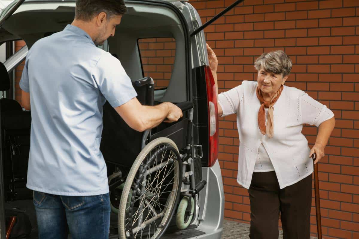 Un taxi spécialisé aide une femme âgée en fauteuil roulant à monter dans une camionnette.